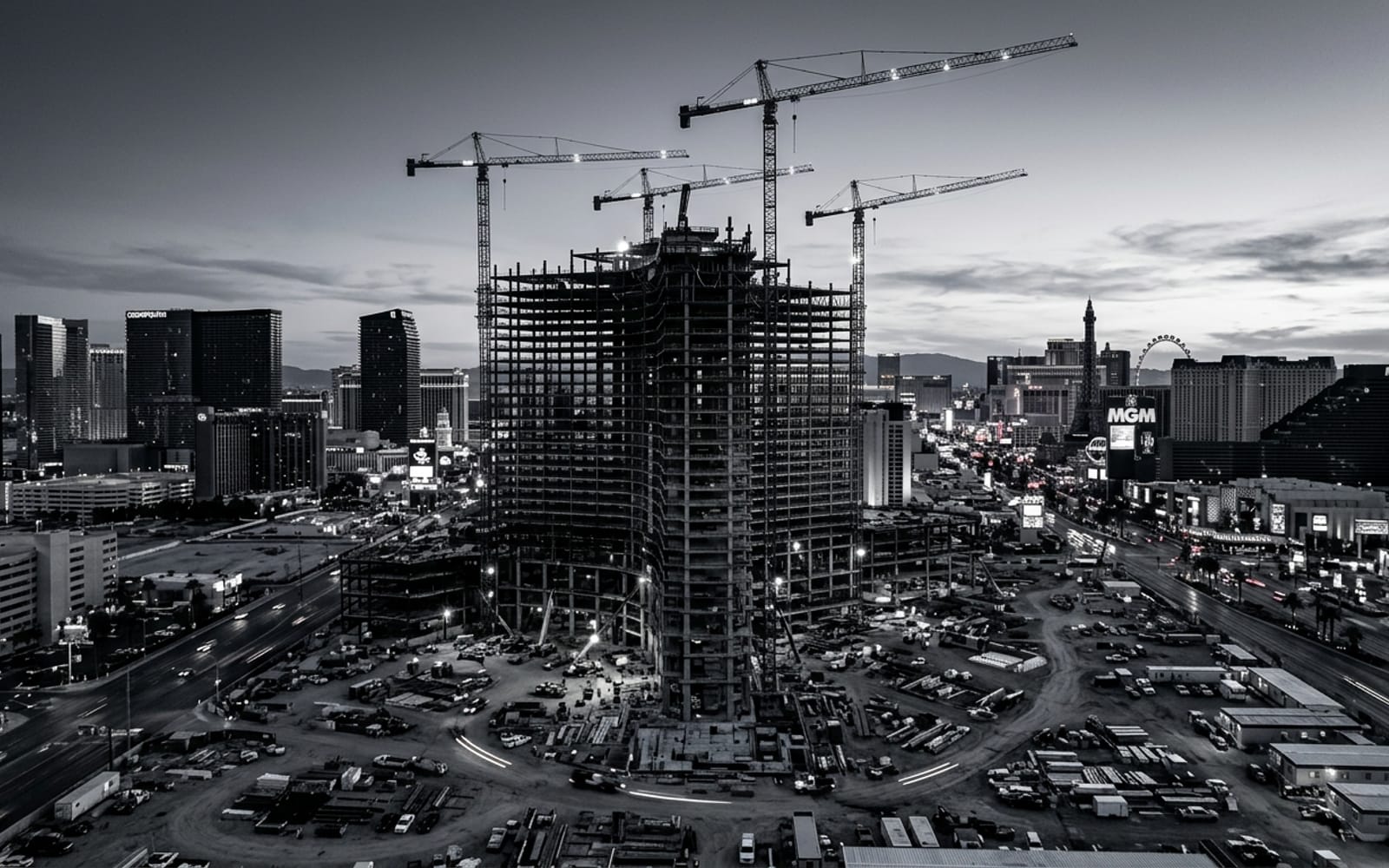 A Las Vegas high-rise construction site at dusk, with tower cranes and exposed steel framework silhouetted against a silver sky.